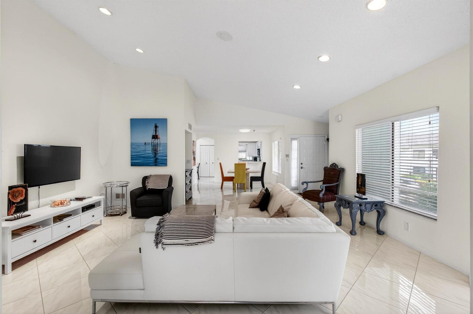 A bright living room with white tile floors, a white sectional sofa, and a television — 7485 Glendevon Lane # 1105, Delray Beach FL 33446, DELRAY BEACH, FL