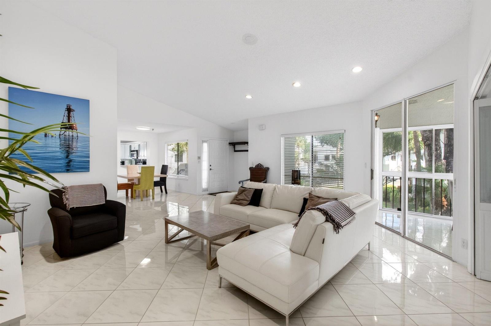A bright living room features white tile floors, a white sectional sofa, and a dark armchair — 7485 Glendevon Lane # 1105, Delray Beach FL 33446, DELRAY BEACH, FL