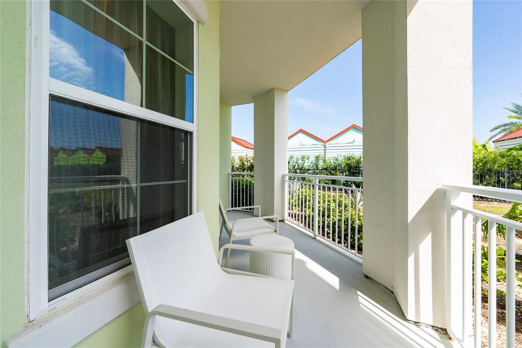 A covered balcony features white chairs, a small table, and white railings overlooking greenery — 8061 VACATION AVENUE UNIT 114, KISSIMMEE, FL