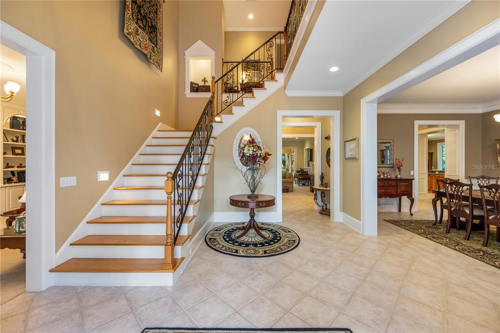 A foyer features a wooden staircase with iron railings, tile flooring, and a round table — 5009 PLEASURE ISLAND ROAD, BELLE ISLE, FL