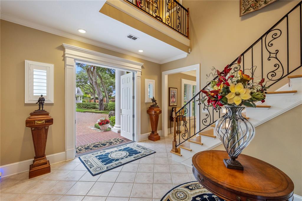 A grand foyer features a tiled floor, a staircase with iron railings, and an open doorway — 5009 PLEASURE ISLAND ROAD, BELLE ISLE, FL
