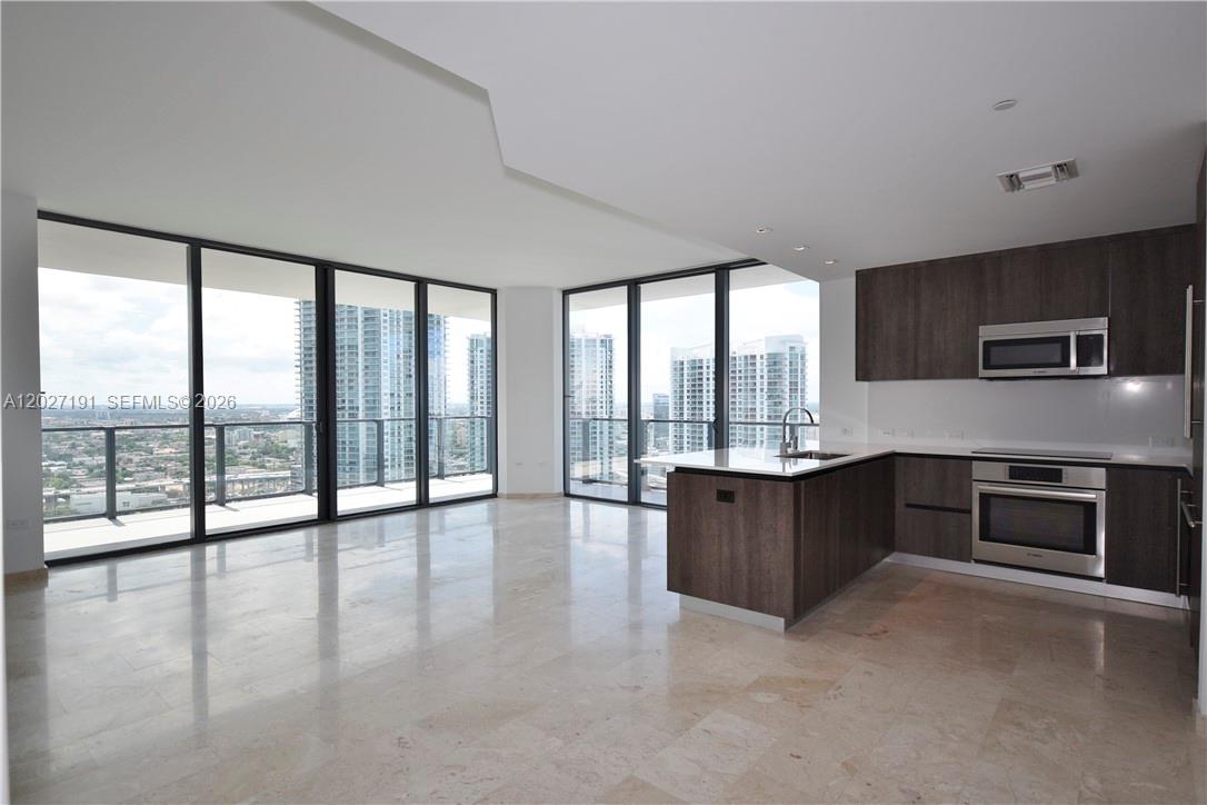 A modern kitchen and living area feature floor-to-ceiling windows, marble floors, and dark cabinetry — 68 SE 6th St # 2812, Miami FL 33131, MIAMI, FL