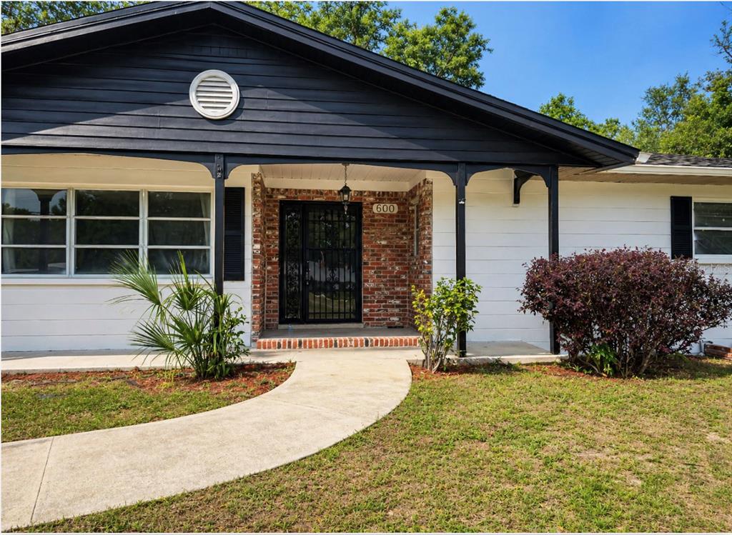 A single-story house with white siding, a brick entryway, and a dark-painted gable roof — 600 NE 53RD COURT, OCALA, FL