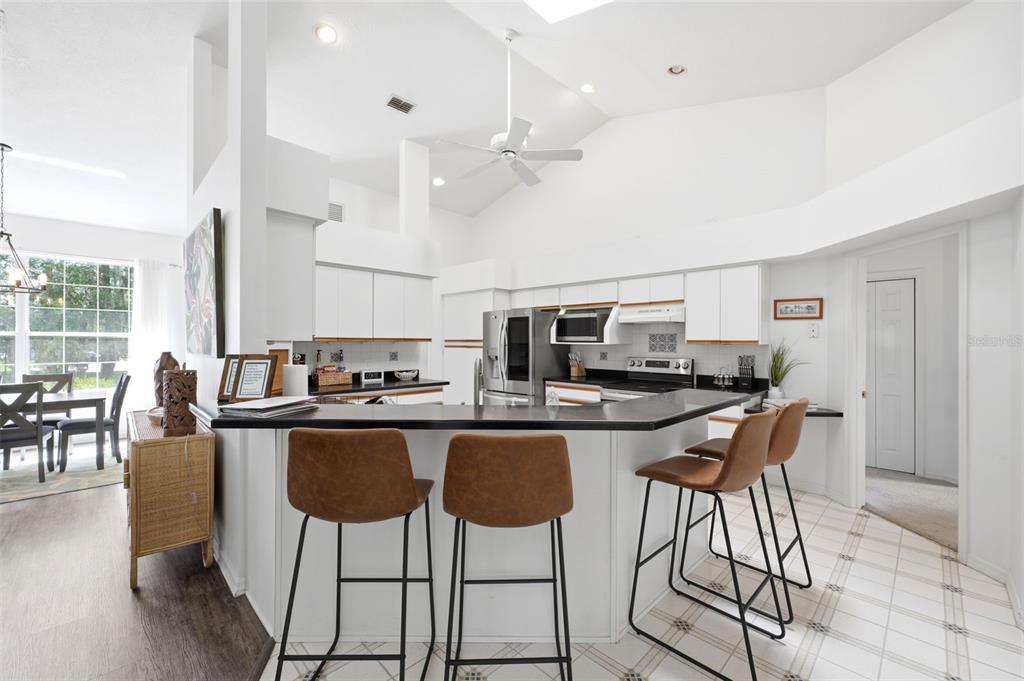A kitchen with white cabinets, black countertops, and three brown bar stools at a peninsula — 240 N COUNTRY CLUB DRIVE, CRYSTAL RIVER, FL