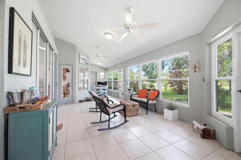 A sunroom with tile flooring, two ceiling fans, wicker furniture, and large windows overlooking greenery — 240 N COUNTRY CLUB DRIVE, CRYSTAL RIVER, FL