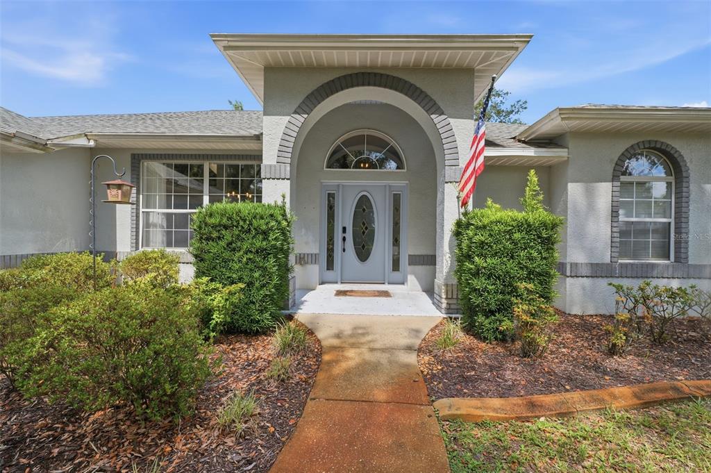 A front view of a single-story house with a covered arched entryway and American flag — 240 N COUNTRY CLUB DRIVE, CRYSTAL RIVER, FL