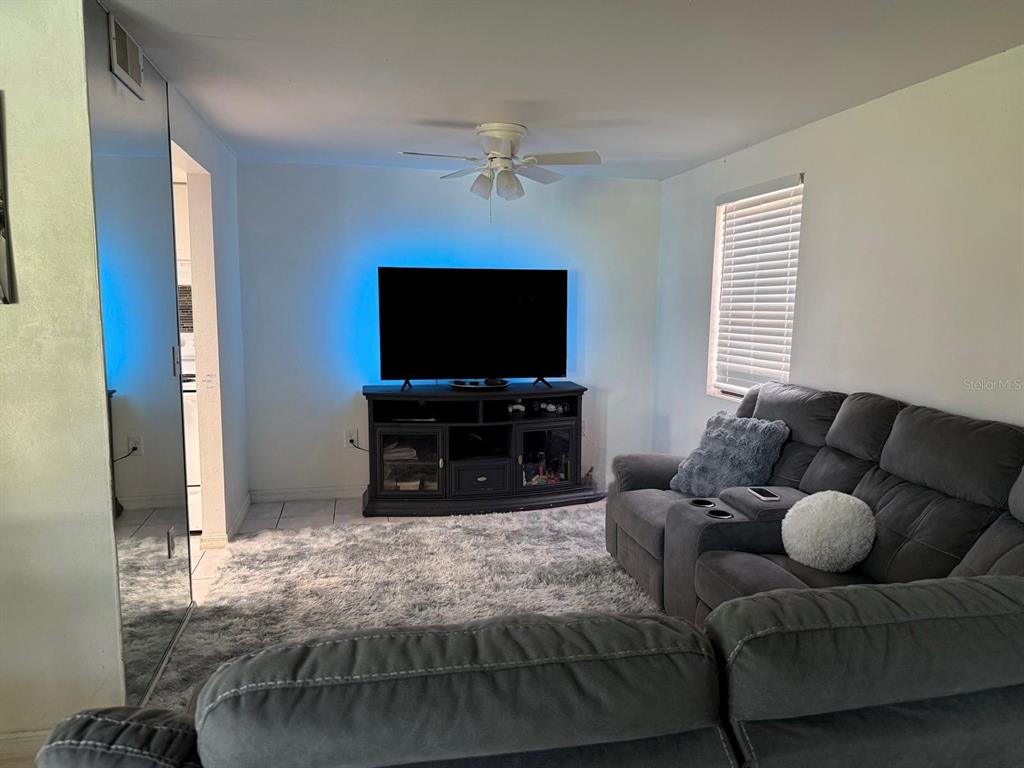 A living room features a gray sectional sofa, a television on a stand, and carpeting — 5026 WATER OAK DRIVE UNIT 114, BRADENTON, FL