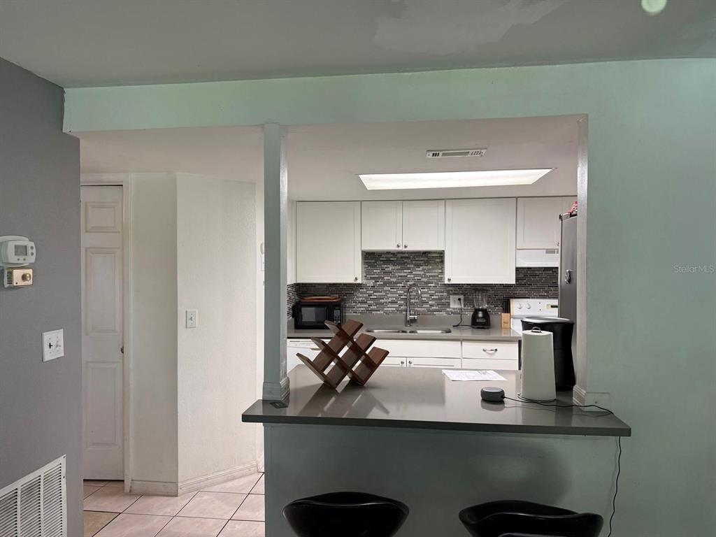 A kitchen with white cabinets and a gray tiled backsplash viewed over a breakfast bar — 5026 WATER OAK DRIVE UNIT 114, BRADENTON, FL