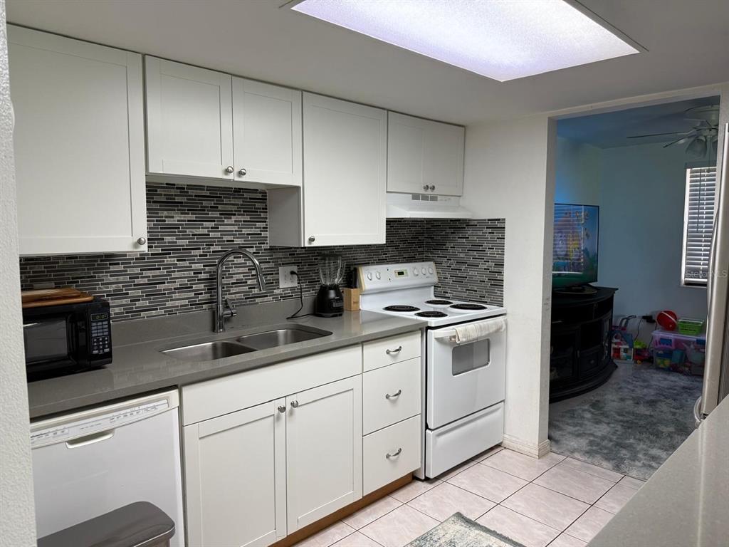 A kitchen features white cabinets, gray countertops, a tiled backsplash, and white appliances — 5026 WATER OAK DRIVE UNIT 114, BRADENTON, FL