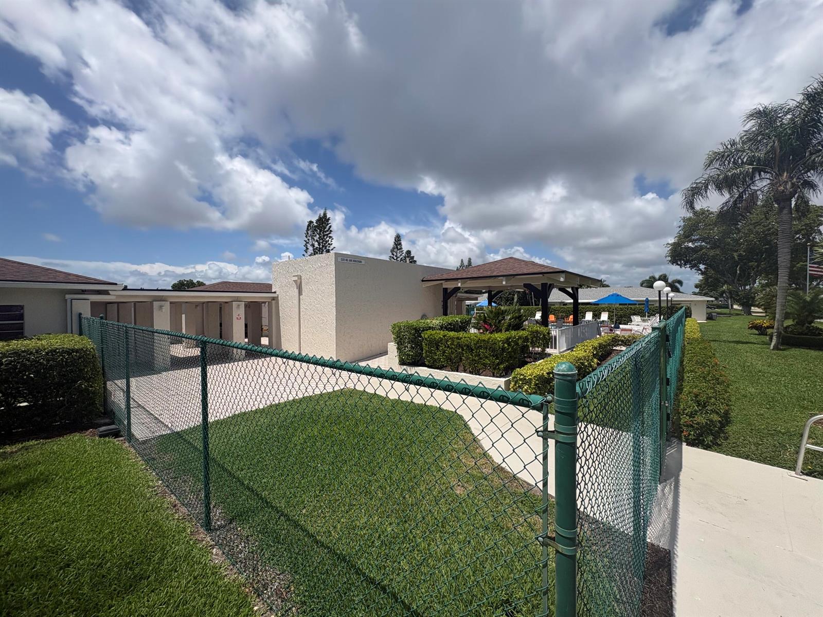 A green chain-link fence surrounds a paved patio area with a gazebo and landscaping — 1020 Silk Oak Terrace # 104, Delray Beach FL 33445, DELRAY BEACH, FL