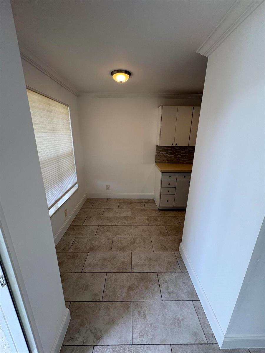 A small room with tiled flooring, a window with blinds, and a small kitchen cabinet unit — 1020 Silk Oak Terrace # 104, Delray Beach FL 33445, DELRAY BEACH, FL