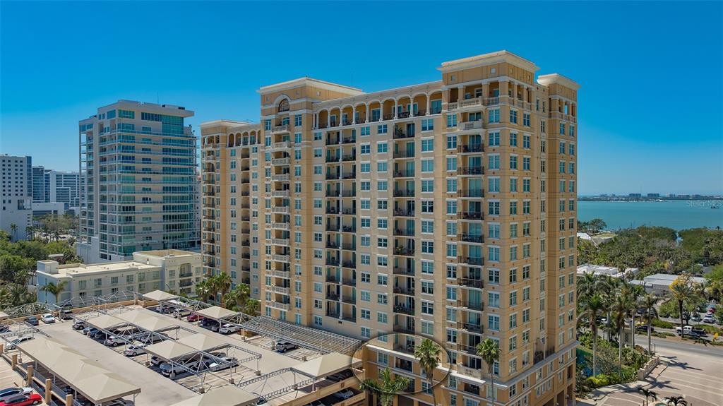 An exterior view of a tall, tan residential building with a parking lot in front — 750 N TAMIAMI TRAIL UNIT 304, SARASOTA, FL