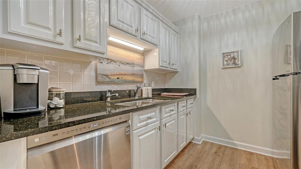 A kitchen features white cabinetry, dark granite countertops, stainless steel appliances, and wood-look flooring — 750 N TAMIAMI TRAIL UNIT 304, SARASOTA, FL