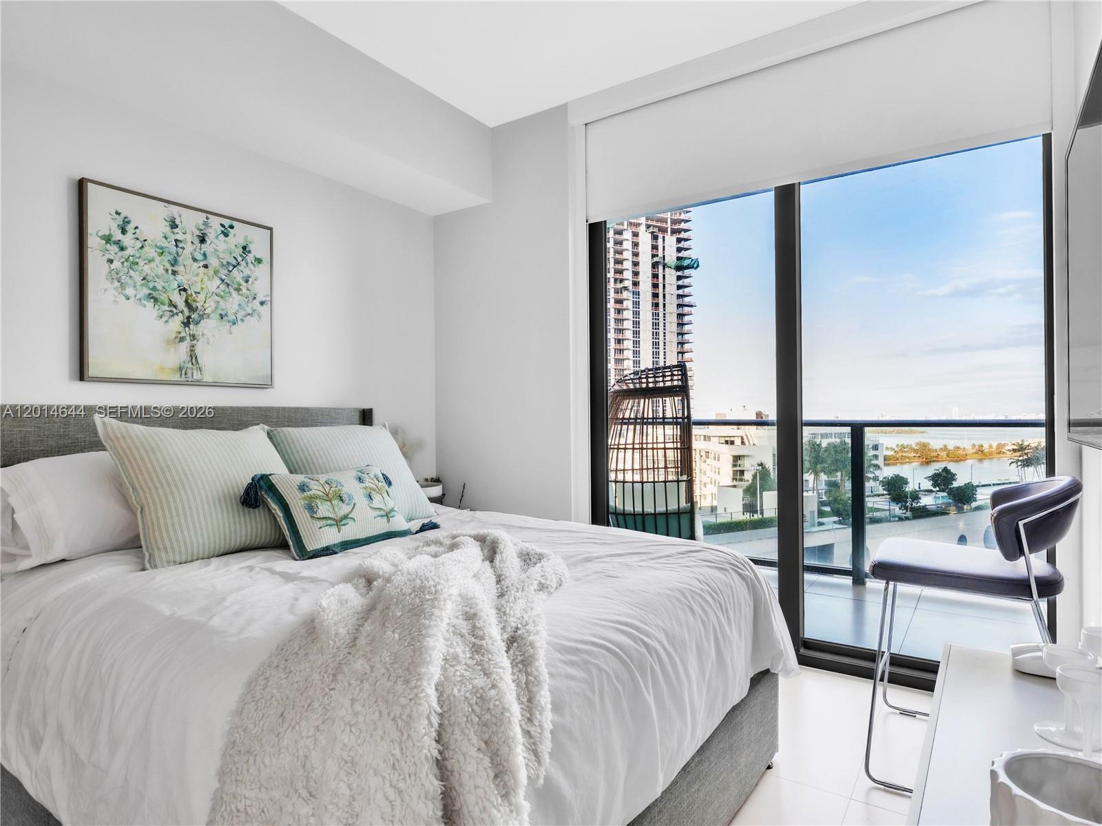 A bedroom features a bed with white bedding, a framed floral painting, and a balcony view — 501 NE 31st St # 1105, Miami FL 33137, MIAMI, FL