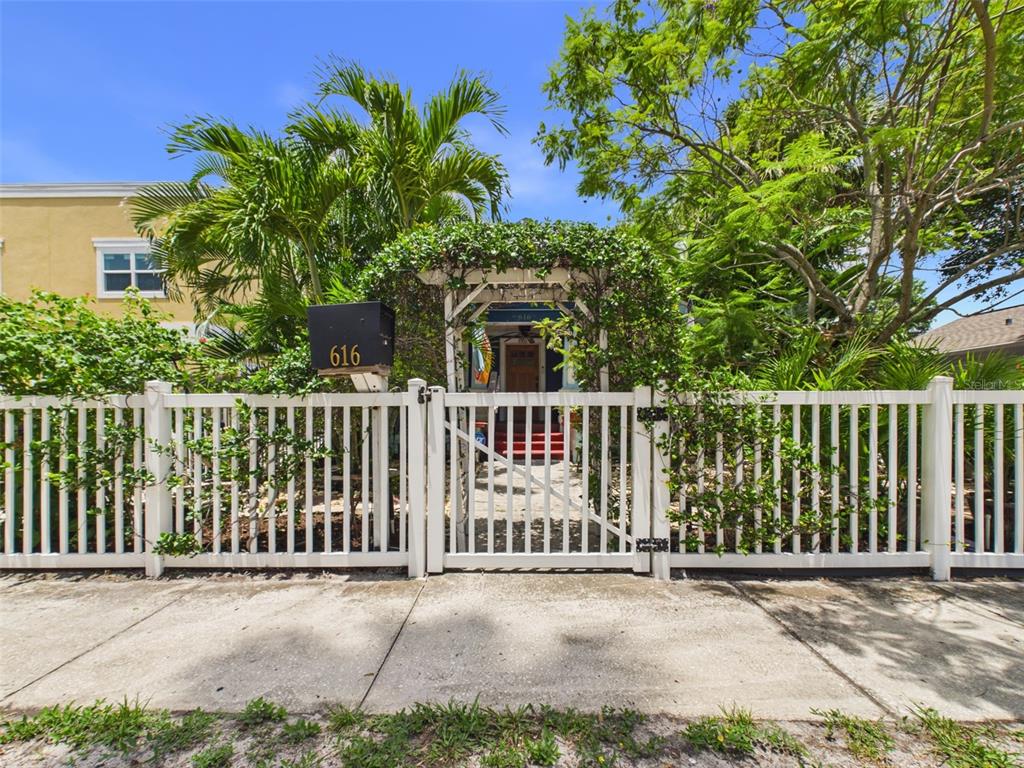 A white picket fence surrounds a house entrance with a vine-covered arbor and palm trees — 616 15TH STREET N, ST PETERSBURG, FL