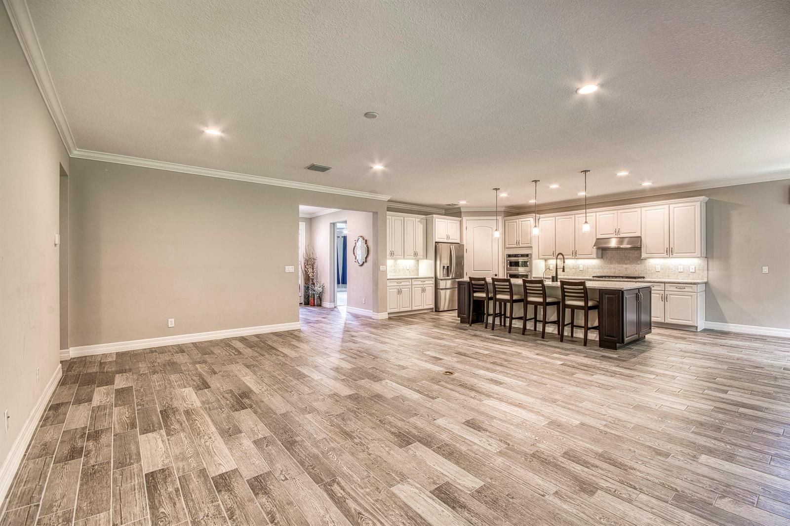 A spacious open-concept kitchen features white cabinetry, a dark island with seating, and wood-look flooring — 134 Shores Pointe Drive, Jupiter FL 33458, JUPITER, FL