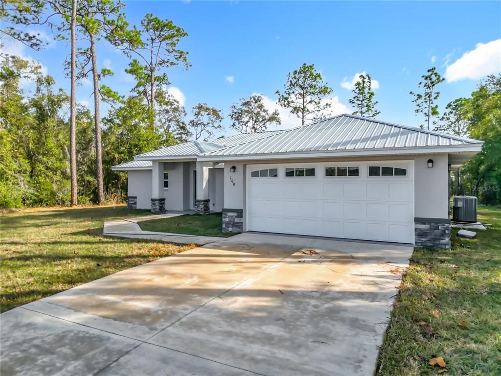 A single-story house with a metal roof, white garage door, and stone accents on the exterior — 168 W CITRUS SPRINGS BOULEVARD, CITRUS SPRINGS, FL