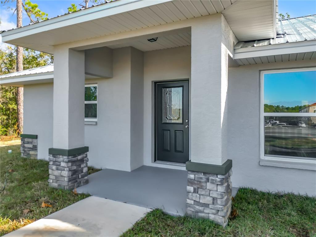 The exterior of a house features a covered porch with stone-based pillars and a dark door — 168 W CITRUS SPRINGS BOULEVARD, CITRUS SPRINGS, FL
