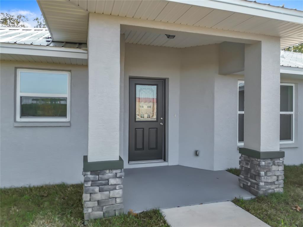 A front porch with a dark door, stone-based columns, and gray stucco exterior walls — 168 W CITRUS SPRINGS BOULEVARD, CITRUS SPRINGS, FL