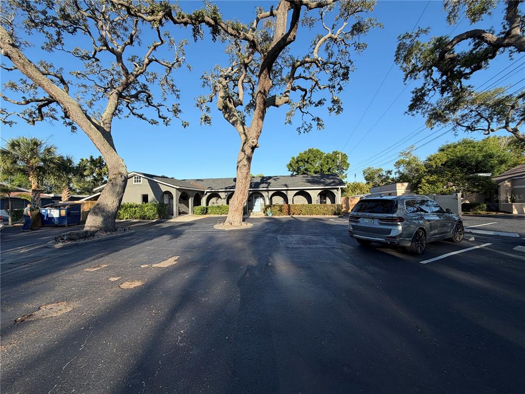 A single-story building with arched entryways sits behind a large parking lot with trees — 11520 OAKHURST ROAD, LARGO, FL