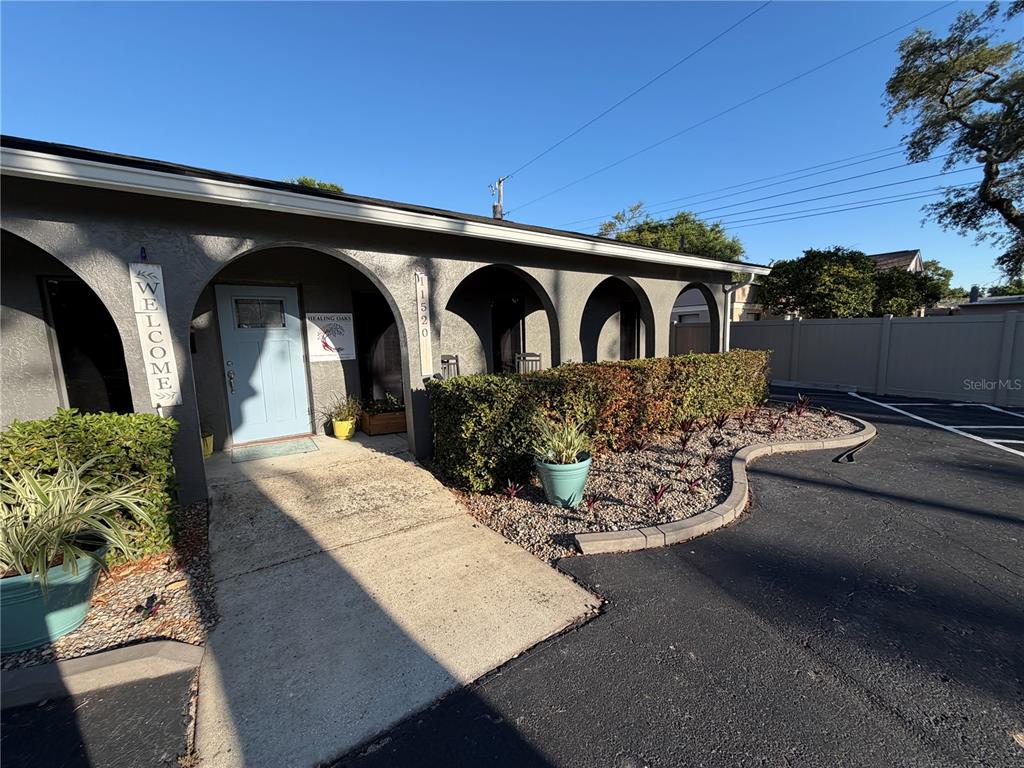 A gray building exterior features arched entryways, a light blue door, and a landscaped front yard — 11520 OAKHURST ROAD, LARGO, FL