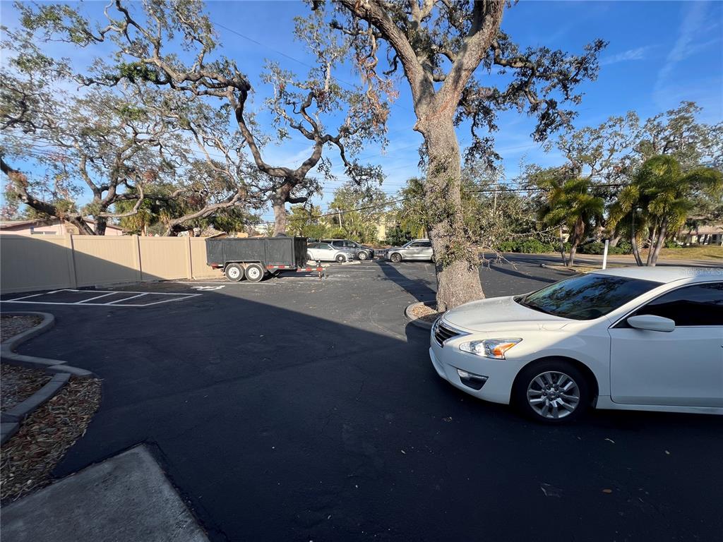 A paved parking lot features a white car, a utility trailer, and several large trees — 11520 OAKHURST ROAD, LARGO, FL
