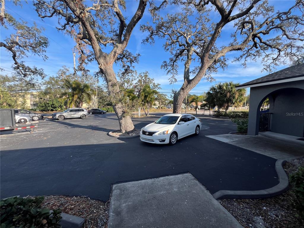 A white sedan is parked in a paved lot shaded by large, mature oak trees — 11520 OAKHURST ROAD, LARGO, FL