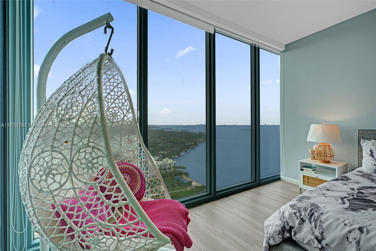A bedroom features a hanging chair, floor-to-ceiling windows, and a view of the water — 601 NE 36th St # 2703, Miami FL 33137, MIAMI, FL