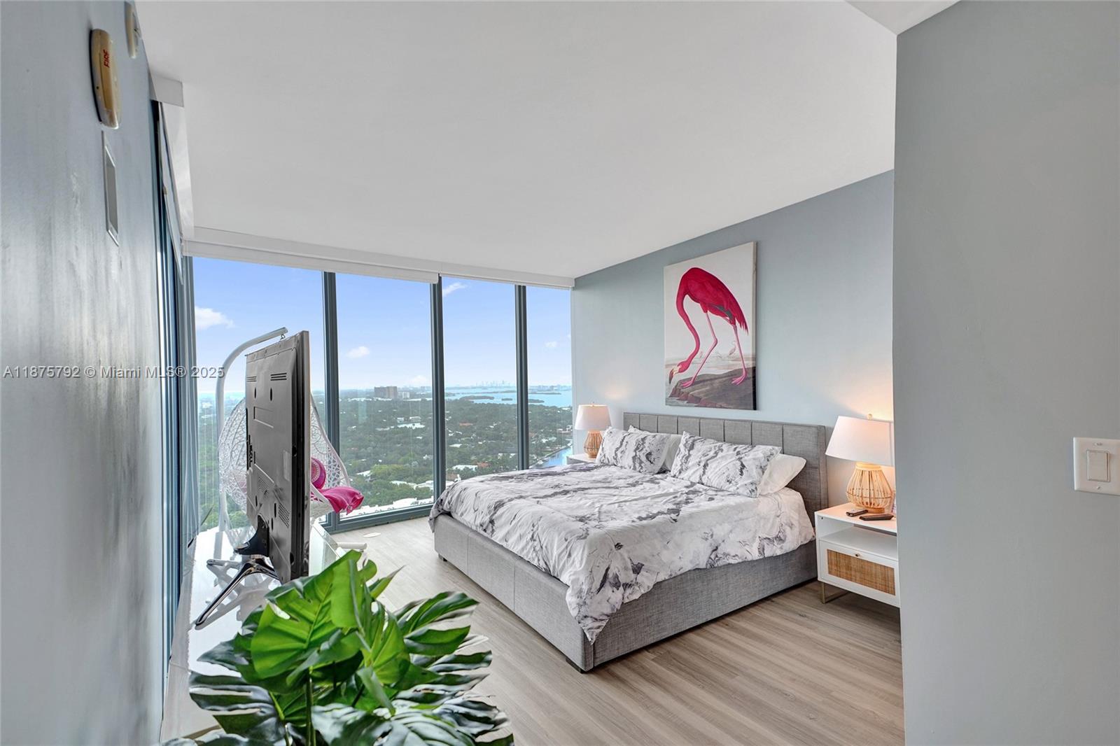 A bedroom features a gray bed, a flamingo painting, and floor-to-ceiling windows with a city view — 601 NE 36th St # 2703, Miami FL 33137, MIAMI, FL
