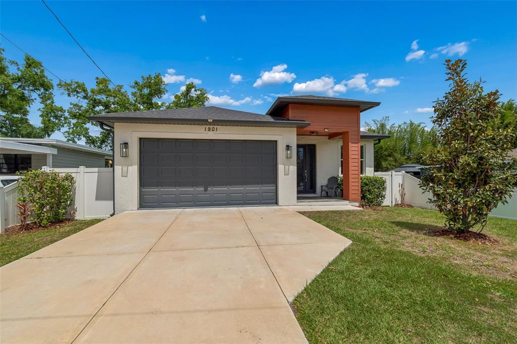 A single-story house with a gray garage door, white stucco walls, and wood-toned accents — 1901 W CLUSTER AVENUE, TAMPA, FL