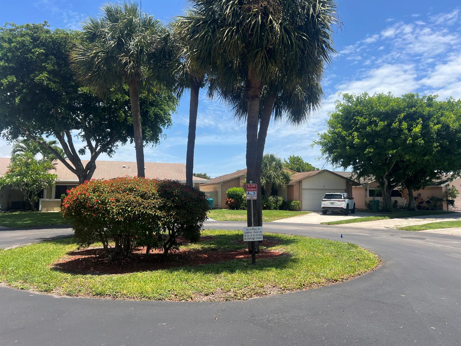 A cul-de-sac features a central landscaped island with palm trees and a slow down sign — 7 Islington Place, Boynton Beach FL 33426, BOYNTON BEACH, FL