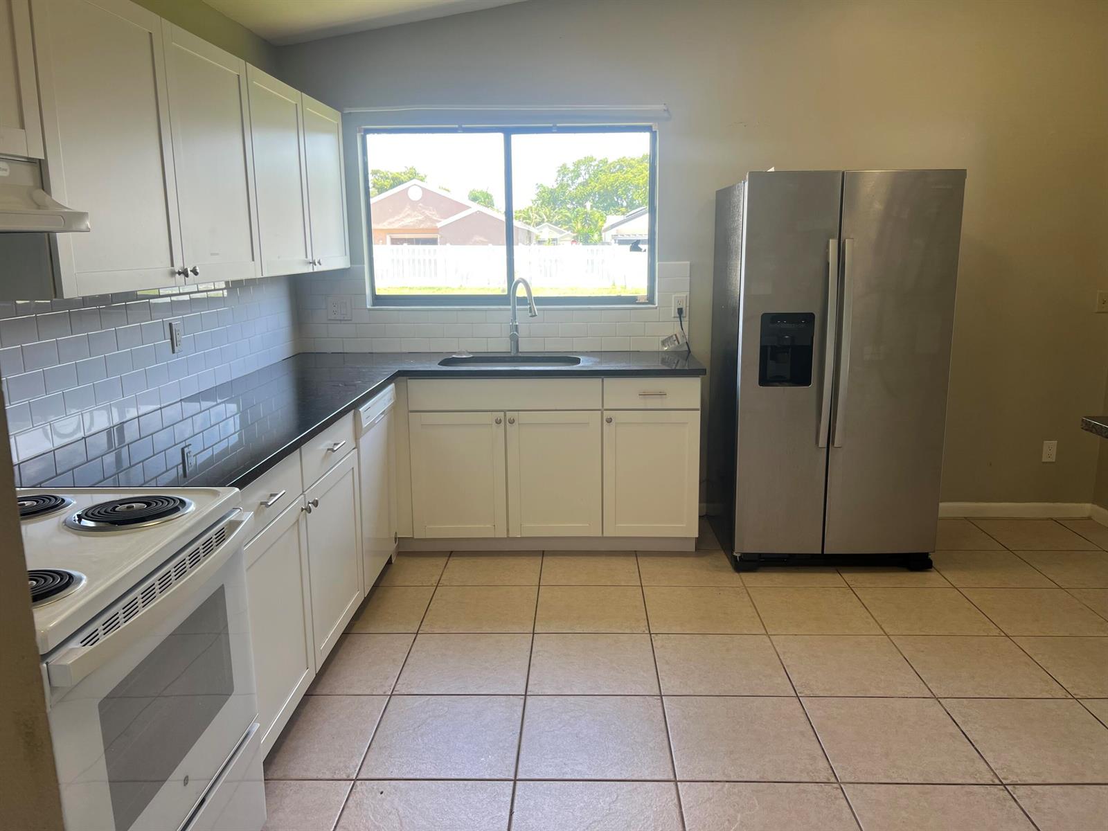 A kitchen features white cabinets, dark countertops, a stainless steel refrigerator, and tiled flooring — 7 Islington Place, Boynton Beach FL 33426, BOYNTON BEACH, FL