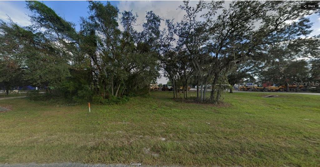 A grassy, undeveloped lot features several mature trees and a view of construction equipment nearby — N/A, POLK CITY, FL