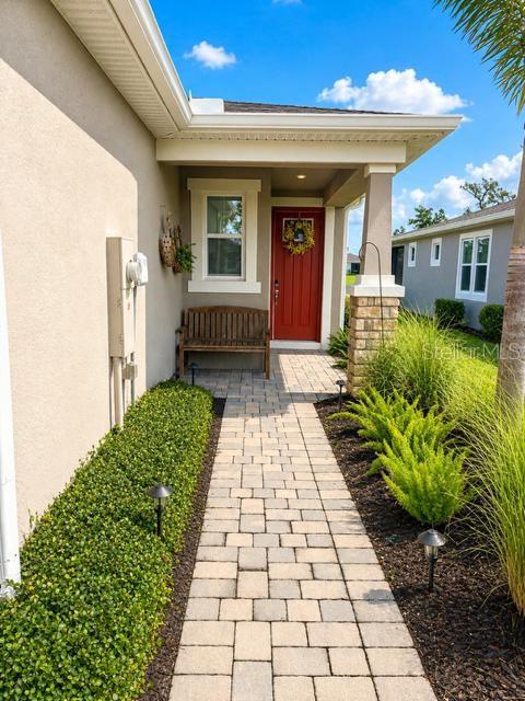 A paved walkway leads to a covered front porch with a wooden bench and red door — 6055 TIMBERDALE AVENUE, WESLEY CHAPEL, FL