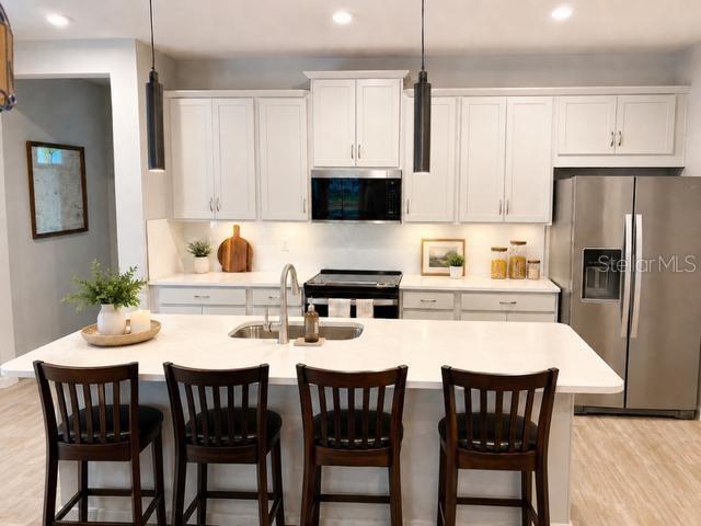 A modern kitchen features white cabinetry, a central island with bar seating, and stainless steel appliances — 6055 TIMBERDALE AVENUE, WESLEY CHAPEL, FL