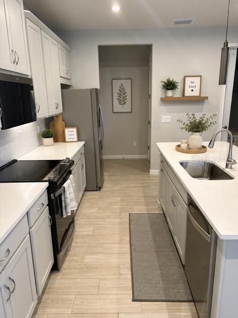 A kitchen features white cabinets, stainless steel appliances, a center island, and light-colored tile flooring — 6055 TIMBERDALE AVENUE, WESLEY CHAPEL, FL