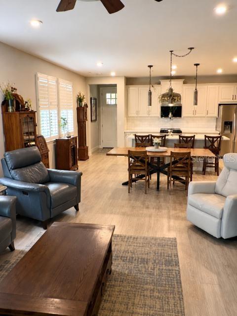 An open-concept living and dining area features light wood flooring, white cabinetry, and pendant lighting — 6055 TIMBERDALE AVENUE, WESLEY CHAPEL, FL