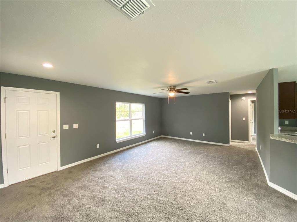 A living room with gray walls, gray carpeting, a ceiling fan, and a white door — 4004 SW 138TH PLACE, OCALA, FL