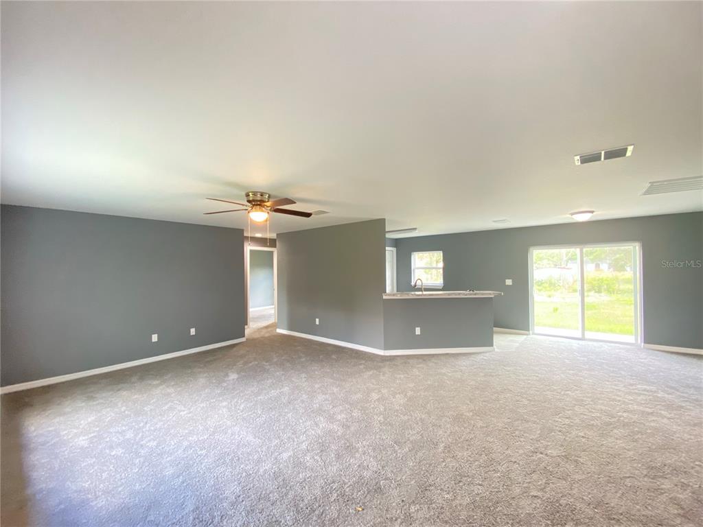 An open-concept living area features gray walls, beige carpeting, a ceiling fan, and a kitchen — 4004 SW 138TH PLACE, OCALA, FL
