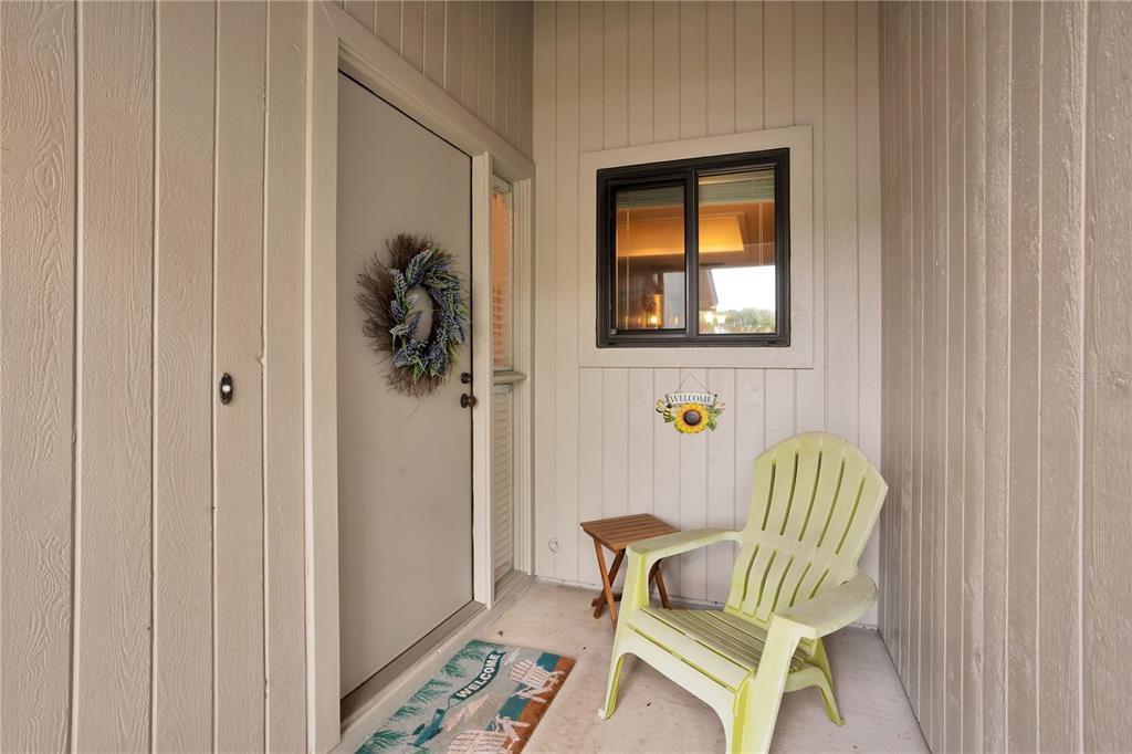 A light-colored front porch features a door with a wreath, a chair, and a mat — 4229 SEA MIST DRIVE, NEW SMYRNA BEACH, FL