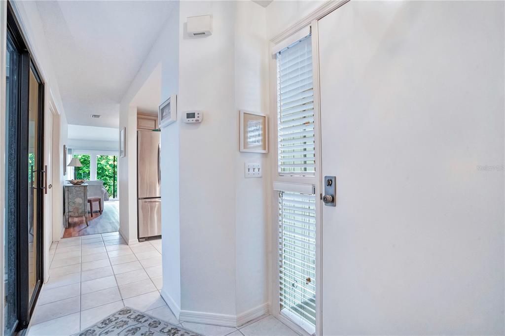 A white door with integrated blinds opens into a tiled hallway leading toward a kitchen — 4229 SEA MIST DRIVE, NEW SMYRNA BEACH, FL