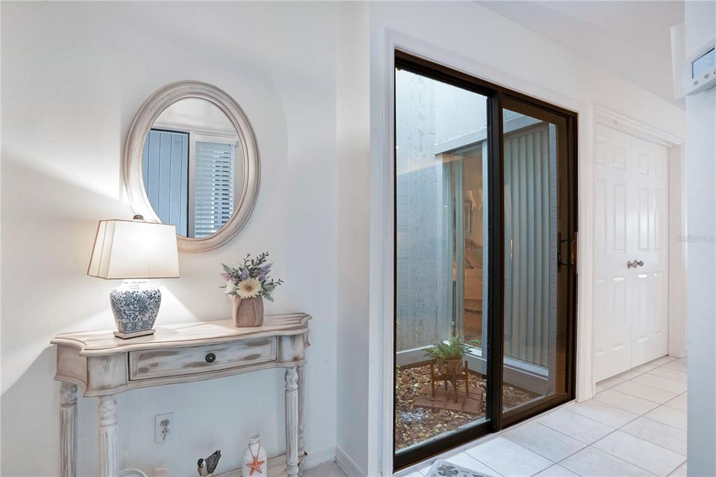 A hallway features a console table with a lamp, an oval mirror, and sliding glass doors — 4229 SEA MIST DRIVE, NEW SMYRNA BEACH, FL