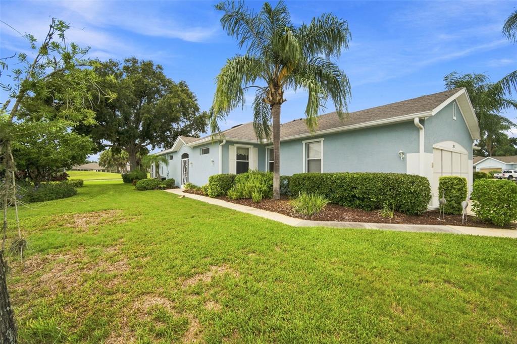 A light blue house with a palm tree and manicured hedges sits on a grassy lawn — 2102 ACADIA GREENS DRIVE UNIT 2102, SUN CITY CENTER, FL