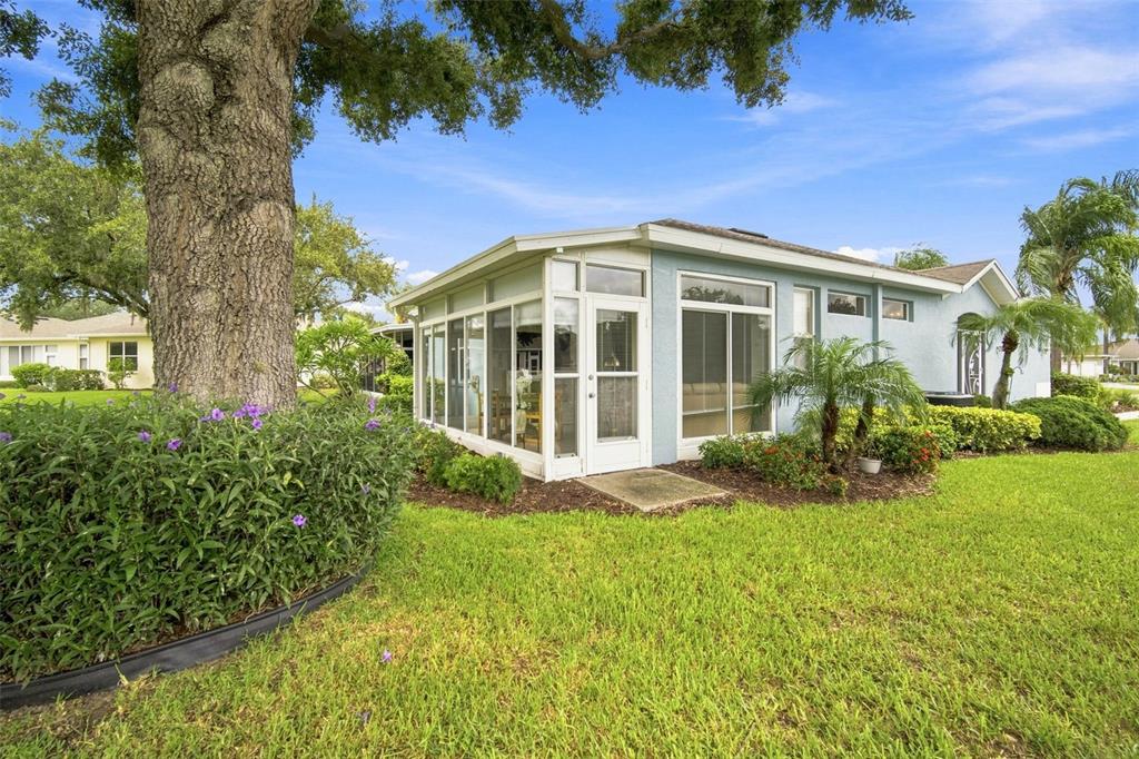 A light blue house with a glass-enclosed sunroom sits on a lawn beside a large tree — 2102 ACADIA GREENS DRIVE UNIT 2102, SUN CITY CENTER, FL