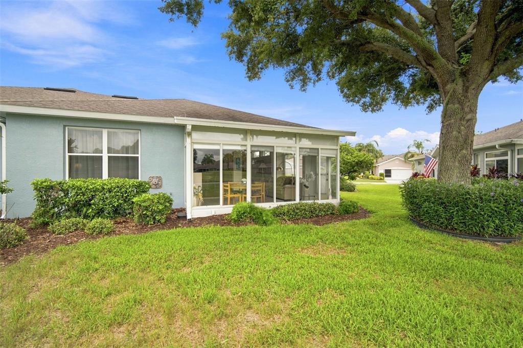 A light blue house features a glass-enclosed sunroom and a large tree in the yard — 2102 ACADIA GREENS DRIVE UNIT 2102, SUN CITY CENTER, FL