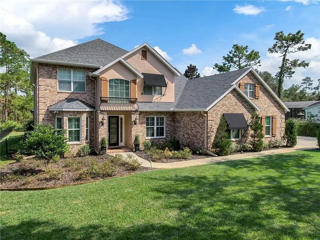 A two-story brick house features a front entrance, multiple windows, and a landscaped lawn — 2660 WINNEMISSETT OAKS DRIVE, DELAND, FL