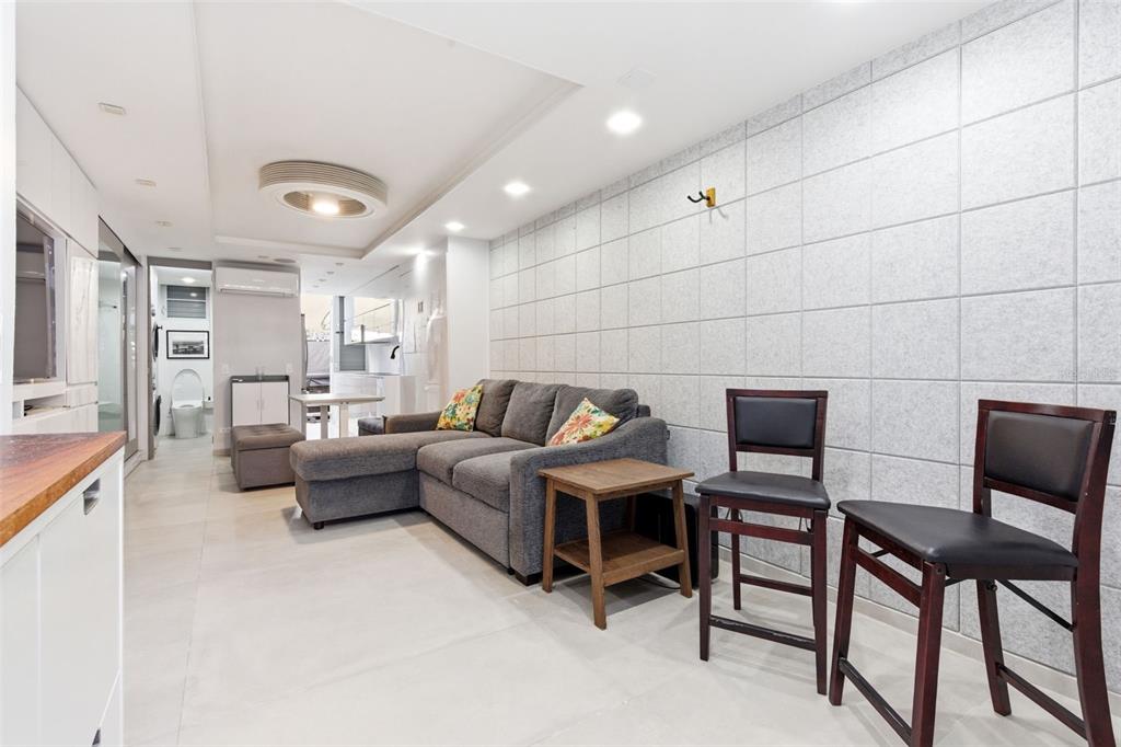 A living room features a grey sectional sofa, two bar stools, and tiled wall panels — 1477 ASHFORD AVENUE UNIT 9A, SAN JUAN, PR