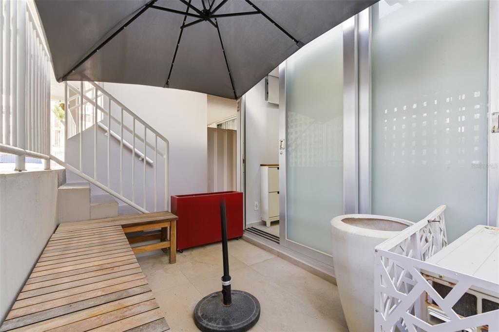 A small outdoor patio features a wooden bench, a red planter, and a patio umbrella — 1477 ASHFORD AVENUE UNIT 9A, SAN JUAN, PR