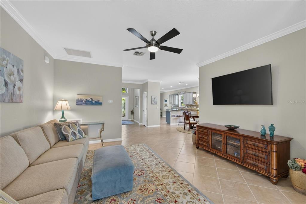 A living room features a beige sofa, a blue ottoman, and a wooden media console — 7031 QUIET CREEK DRIVE, BRADENTON, FL