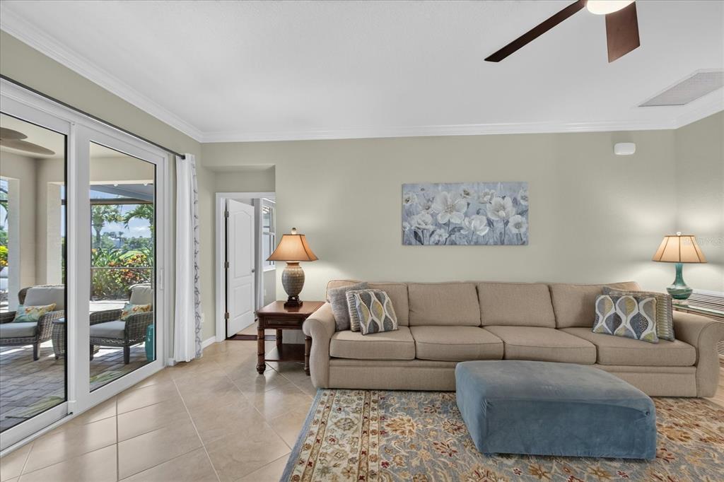 A living room features a beige sectional sofa, blue ottoman, area rug, and sliding glass doors — 7031 QUIET CREEK DRIVE, BRADENTON, FL